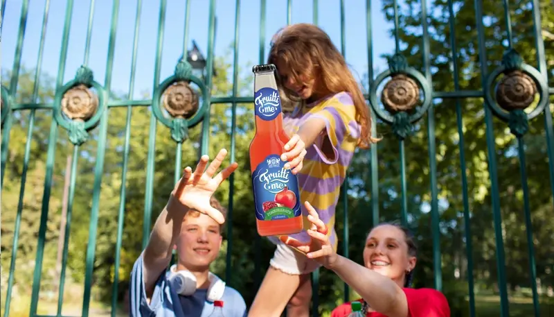 Group of happy friends sharing a Fruitti Me juice bottle outdoors.