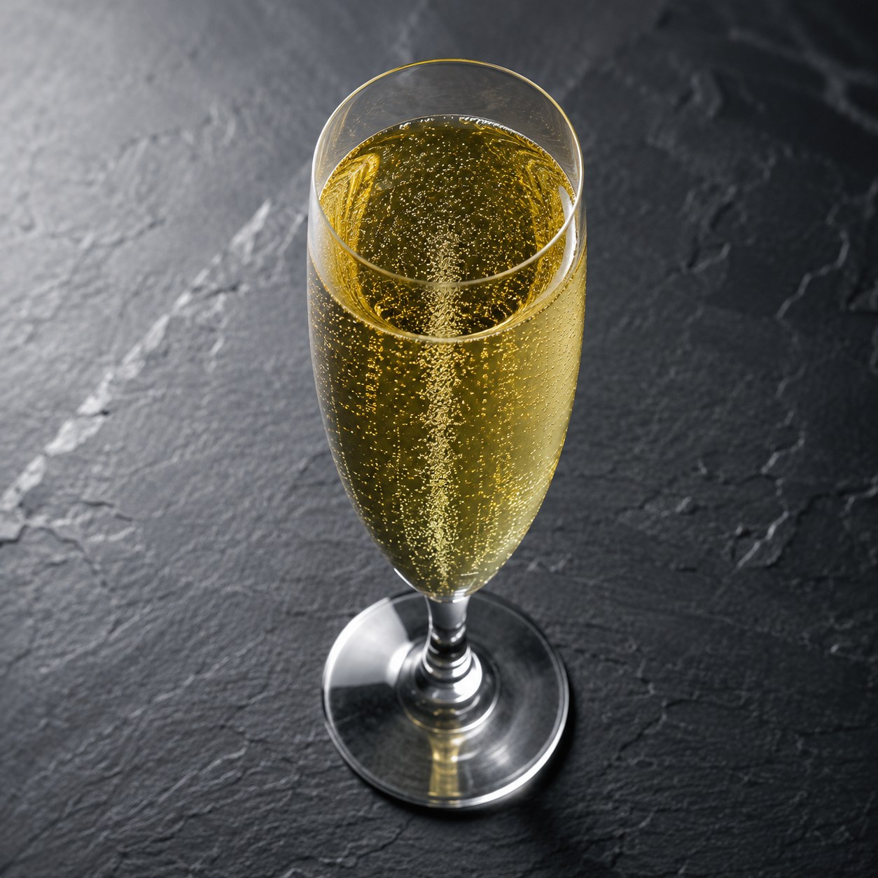 Glass flute filled with sparkling green tea and fine bubbles on a slate surface